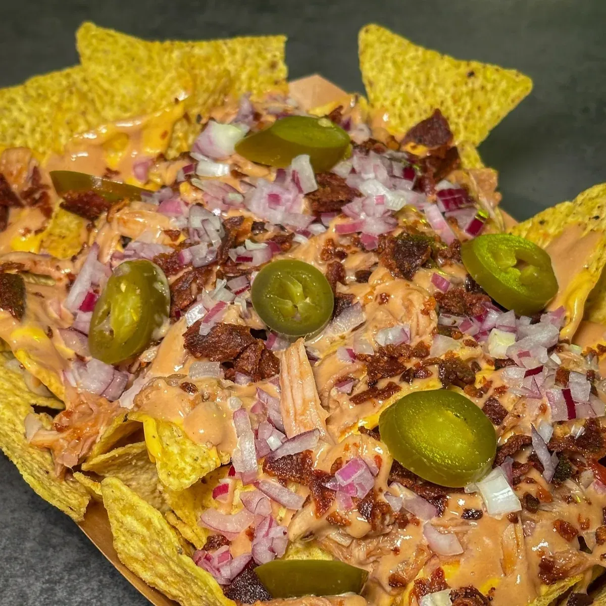 Nachos desde arriba con pulled pork, bacon, jalapeños, cebolla morada y salsa de queso