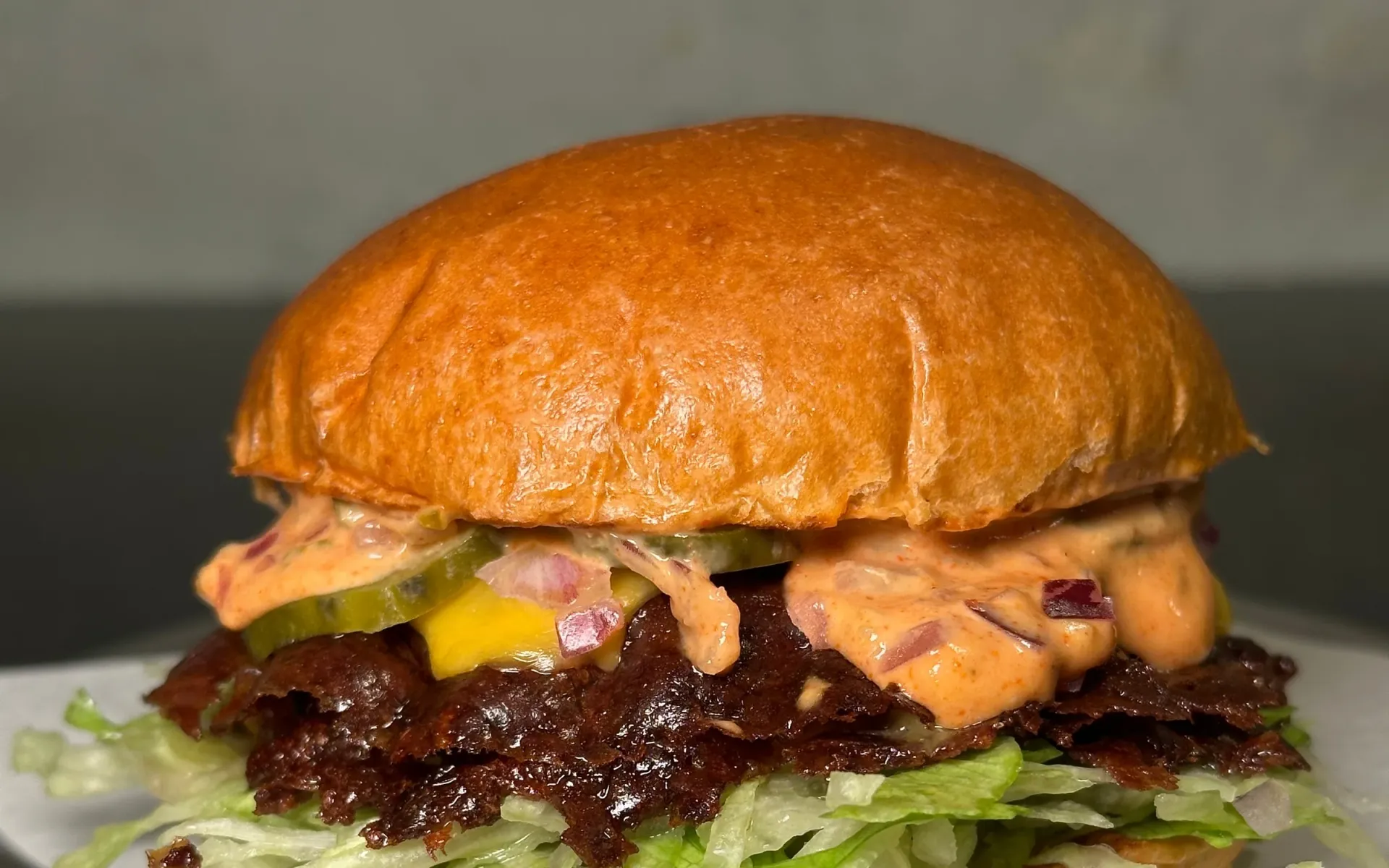 Hamburguesa con lechuga, salsa rosa con cebolla morada y pepinillos, sobre papel de Duality y bandeja de metal