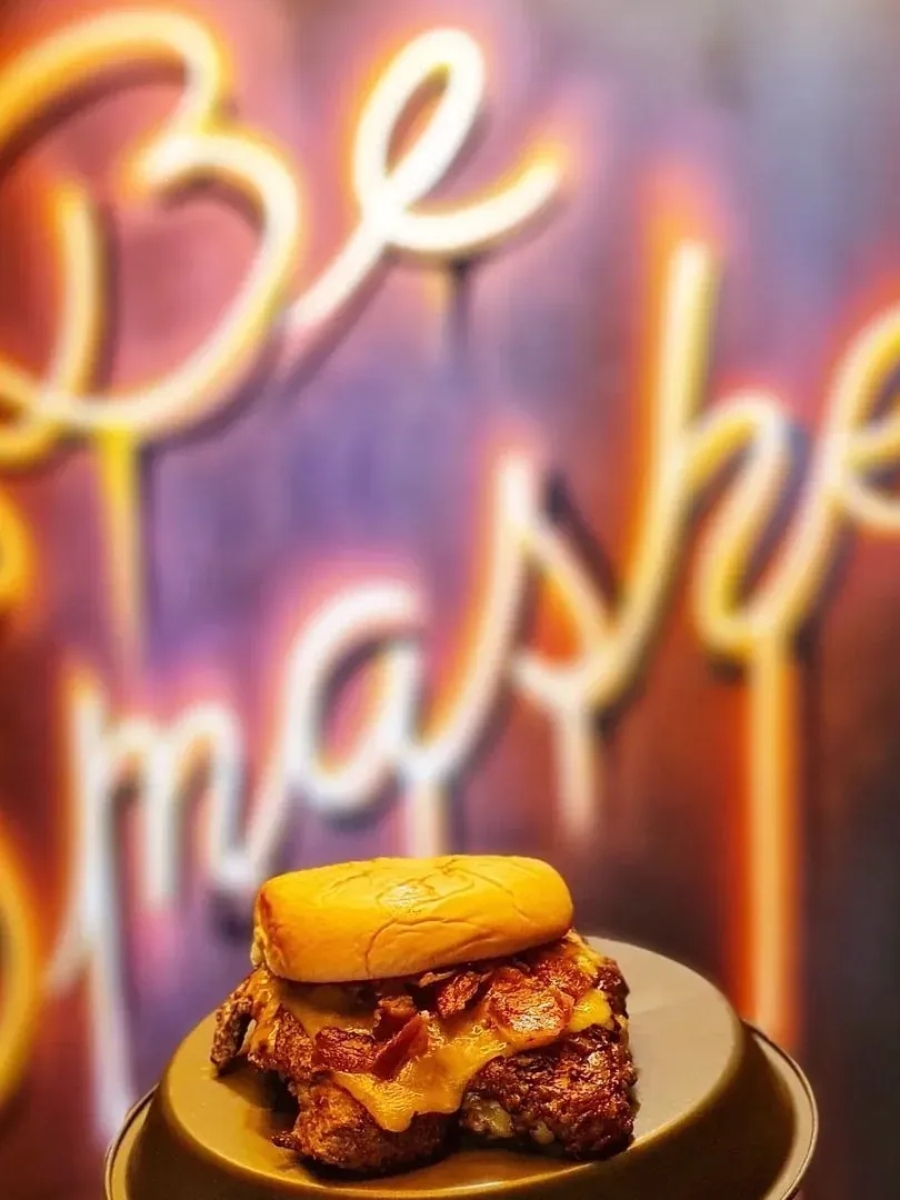 Hamburguesa con queso fundido en un plato, delante de un rótulo de neón naranja en letra cursiva