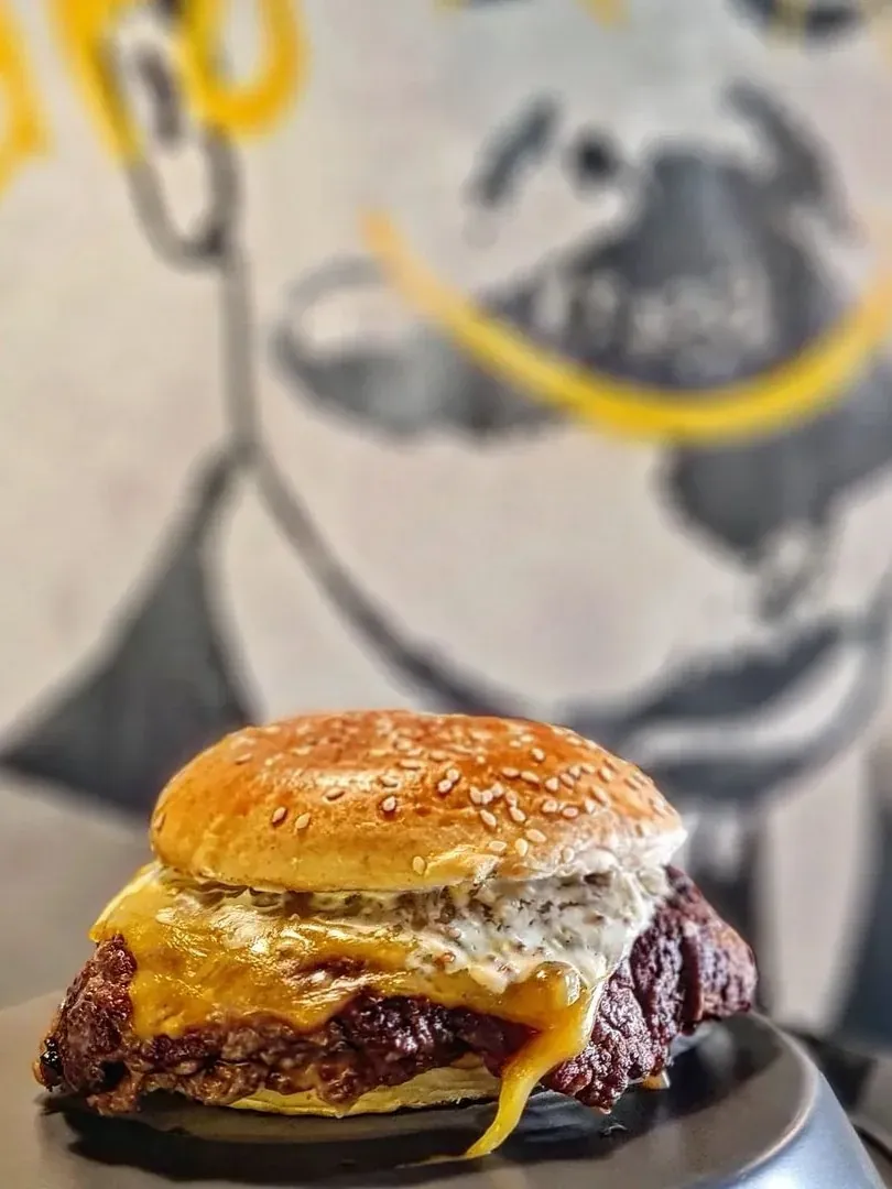 Hamburguesa con pan de sésamo, cheddar y salsa blanca delante del mural con bigote